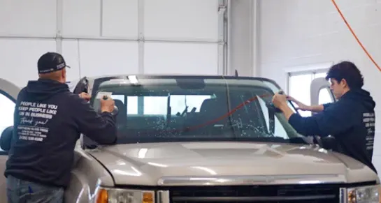 Two men replacing a broken windshield on a pickup truck.