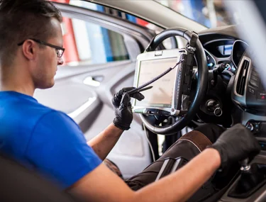 Man with a computer in the drivers seat of a car calibrating the ADAS system.