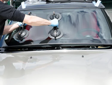 Glass repair tech pulling the windshield off a car with two pairs of giant suction cups.