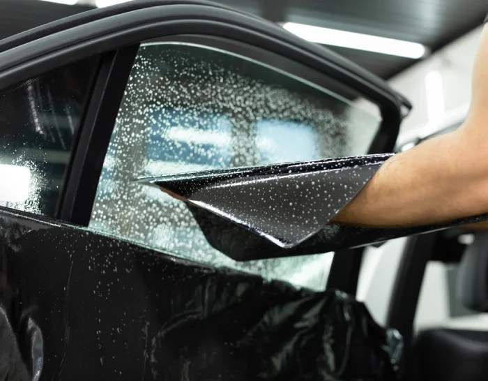 Expert glass tinter applying tint to side car window.