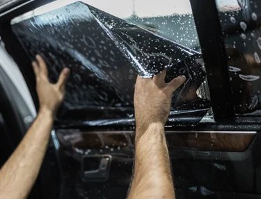 Close up of a man applying window tinting treatment to the side window of a car.