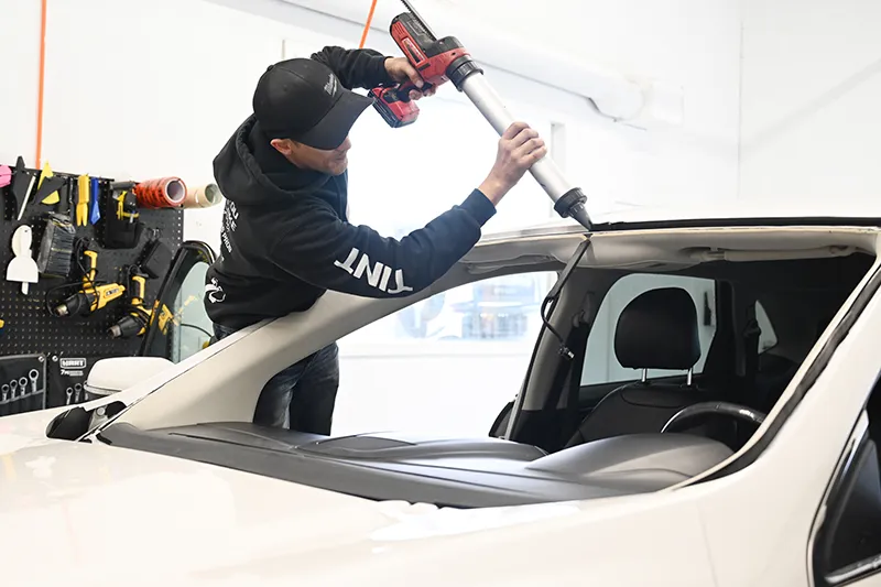 Man sealing a newly installed windshield on a car.